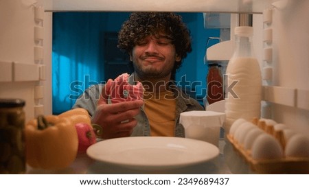 Point of view POV from inside refrigerator hungry Indian man Arabian guy male at night kitchen open fridge want eat take bitten sweet donut smiling condemn bakery unhealthy food nutrition overeating Royalty-Free Stock Photo #2349689437