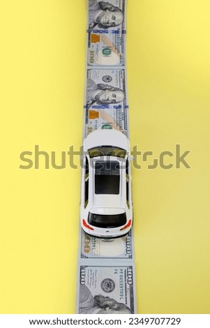 White toy car on money road on yellow background.