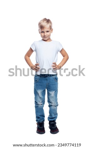 Smiling boy stands with his hands on his belt. Blond guy in a white t-shirt and jeans. Full height. Isolated on a white background. Vertical.