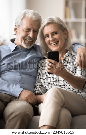 Cheerful old retired husband and wife using smartphone together, talking on family conference video call, enjoying distant online communication, modern Internet technology. Vertical shot