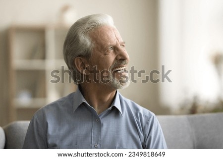 Cheerful dreamy older retired man planning happy retirement, thinking, dreaming, looking away with toothy smile, enjoying good health, leisure, comfort at home. Casual portrait