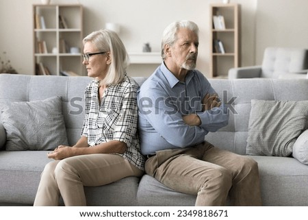 Annoyed ignoring senior couple sitting on home couch back to back, looking away, keeping silence after arguing, thinking on breakup, separation, relationship problems, conflict Royalty-Free Stock Photo #2349818671