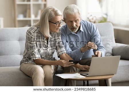 Serious senior married couple calculating domestic expenses, budget, fees, using online financial application on laptop for paying bills. Mature wife showing calculator to concerned elder husband Royalty-Free Stock Photo #2349818685