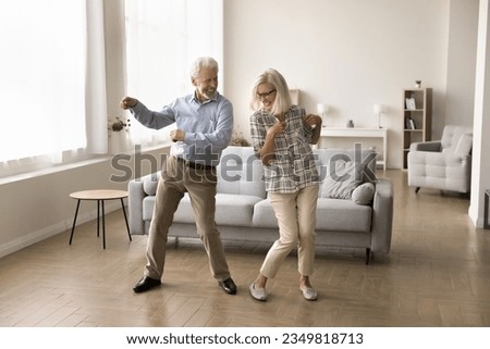 Cheerful active retired elder dancing to disco music in spacious living room, having fun, enjoying sportive hobby, home party, celebrating anniversary, family special date Royalty-Free Stock Photo #2349818713