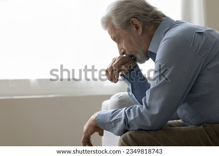 Depressed elder retired man sitting on home couch, looking down, thinking on retirement, healthcare problems, depression, feeling lonely, anxious, suffering from apathy, anxiety, loneliness Royalty-Free Stock Photo #2349818743