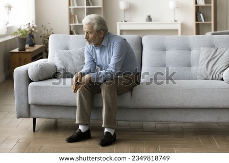 Sad lonely old grey haired man sitting alone on home sofa, looking down in bad thought, suffering from depression, apathy, coping with loss, bad news about healthcare, family problems Royalty-Free Stock Photo #2349818749