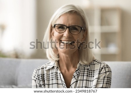 Cheerful beautiful blonde mature woman in trendy eyeglasses and casual shirt looking at camera, smiling, showing white teeth. Happy senior freelance business lady head shot video call portrait Royalty-Free Stock Photo #2349818767