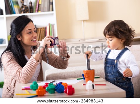 Mother taking a picture of her baby girl.They playing with toys in living room.