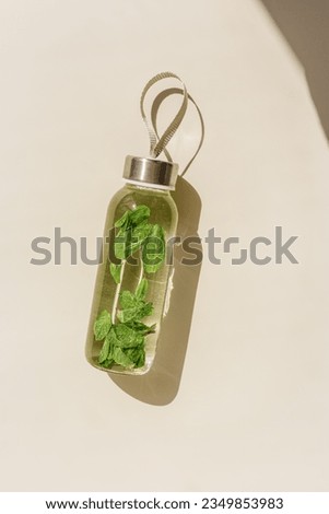 Water drink detox with green mint leaves in glass bottle at sunlight on beige background. Wellness, diet, eating healthy concept. Stylish glass reusable water bottle, lifestyle minimal trend photo Royalty-Free Stock Photo #2349853983