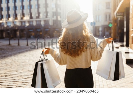 Smiling stylish woman in a hat with shopping bags walks through the streets of Europe on a sunny day. Consumerism, purchases, sale. Lifestyle. Royalty-Free Stock Photo #2349859465
