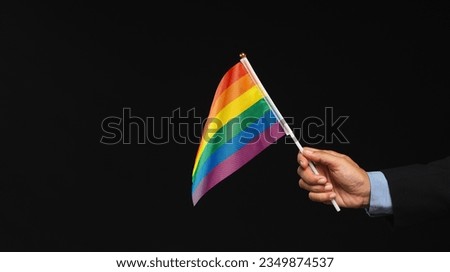 Close-up of a hand holding a rainbow flag while standing on a black background. Calling on all people to support and respect diversity, gender, and human rights and celebrate LGBTQ Pride month. Royalty-Free Stock Photo #2349874537