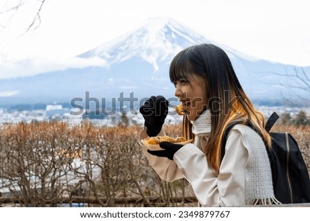Asian woman eating Japanese street food Takoyaki during travel lake Kawaguchi and Mt Fuji. Attractive girl enjoy outdoor lifestyle travel Japan landmark famous place on winter holiday vacation. Royalty-Free Stock Photo #2349879767
