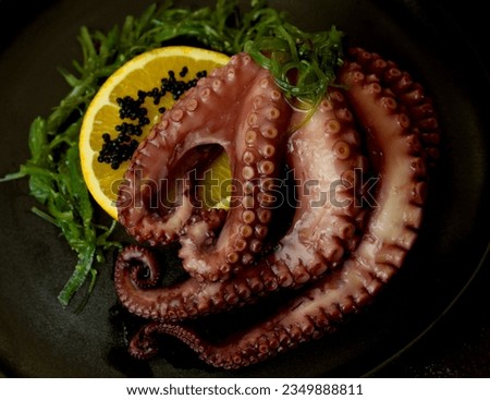 Octopus with orange slice, seaweed salad and black caviar, in a black plate in professional studio lighting. Gourmet style plating. Color contrast. Top view