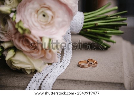 Wedding rings bride and groom with bridal bouquet white and pink flowers roses. Two beautiful golden wedding rings. Mens, womens ring with ornament. Close Up. Engagement.