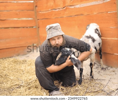 A man in a panama hat with a beard with a goat of the Nubian breed in the summer on a farm