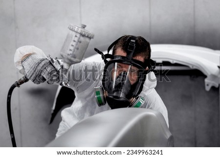 Mechanic man in white costume cloth wearing chemical protective mask while working with painting tool, auto mechanic painting a car, fixing repairing vehicle at garage automobile repair service shop.  Royalty-Free Stock Photo #2349963241