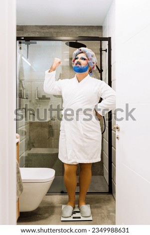 Full length of angry Drag Queen wearing white bathrobe and standing on scales and cursing in bathroom Royalty-Free Stock Photo #2349988631