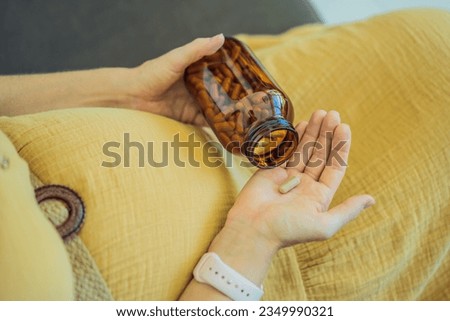 Prenatal Vitamins. Portrait Of Beautiful Smiling Pregnant Woman Holding Transparent Glass Jar With Pills, Taking Supplements For Healthy Pregnancy While Sitting On Couch At Home, Free Space Royalty-Free Stock Photo #2349990321
