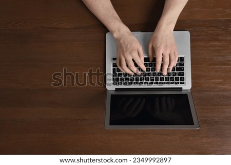 Man working with laptop at wooden table, top view. Space for text