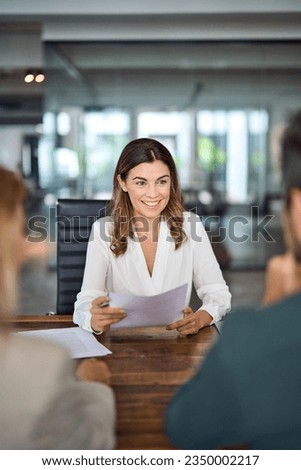 Smiling mature professional business woman banking loan manager, insurance agent, lawyer or financial advisor consulting clients couple sitting at work corporate office meeting. Vertical Royalty-Free Stock Photo #2350002217