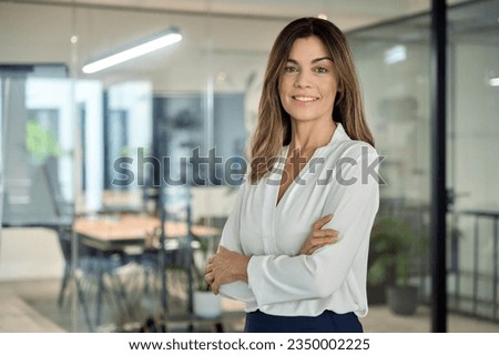 Smiling confident 45 years old Latin professional middle aged business woman corporate leader, happy mature female executive, lady manager standing in office arms crossed looking at camera, portrait. Royalty-Free Stock Photo #2350002225