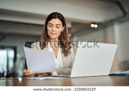 Busy 40 years old business woman working in office checking documents. Mid aged businesswoman accounting manager executive or lawyer using laptop reading paper file financial report, tax invoice. Royalty-Free Stock Photo #2350002229