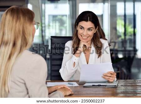 Happy mid aged professional business woman executive hr manager having job interview or business discussion with female applicant holding cv sitting at workplace in corporate office meeting. Royalty-Free Stock Photo #2350002237
