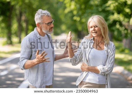 Older Couple Conflicts. Mature Spouses Arguing While Walking In Park, Angry Senior Man And Woman Quarreling Outdoors, Suffering Misunderstanding And Marital Crisis, Wife Making Stop Gesture With Hand Royalty-Free Stock Photo #2350004963