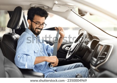 Happy cheerful handsome bearded young hindu man wearing casual outfit driver sitting in front seat, fasten seat belt, driving his brand new nice car and smiling, copy space. Safety driving concept Royalty-Free Stock Photo #2350004969