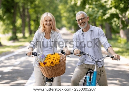Portrait Of Positive Mature Couple Cycling Together In Summer Park, Happy Cheerful Senior Spouses Smiling At Camera, Posing Outdoors While Riding Bicycles, Having Fun, Enjoying Active Lifestyle