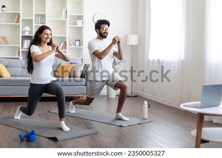 Training At Home. Sporty indian couple doing glutes exercise in front of laptop, happy young eastern spouses watching online tutorials and exercising in living room, practicing sports together Royalty-Free Stock Photo #2350005327