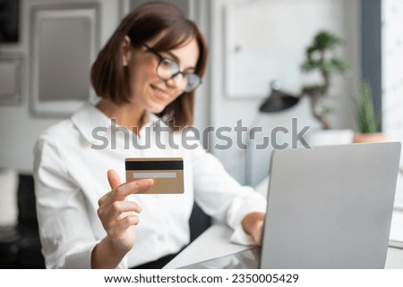 Glad european woman typing on laptop, using credit card, enjoy online shopping and paying for order remotely, sitting in office, selective focus. Sale, banking and cashback