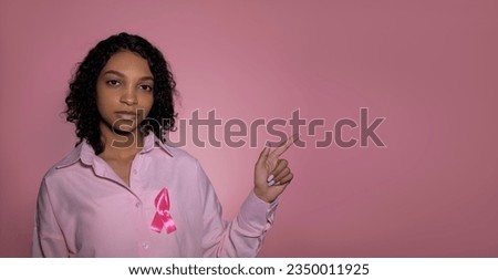 Breast cancer concept. Young girl in pink shirt with ribbon pointing at empty space.Copy space banner