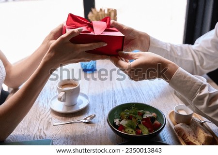 Woman presenting red giftbox with bow to her beloved man