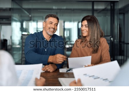 Happy older Latin company executive project manager planning strategy discussing financial or marketing report with diverse business team people in office working at group meeting consulting clients. Royalty-Free Stock Photo #2350017511