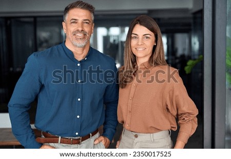 Two happy confident professional mature middle aged Latin business man and business woman corporate executive leaders company managers standing in office looking at camera, portrait.