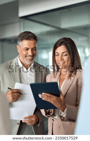Busy smiling executive business team using tablet holding papes standing in office. Professional leaders managers and people workers discussing digital financial project working in teamwork. Vertical Royalty-Free Stock Photo #2350017529