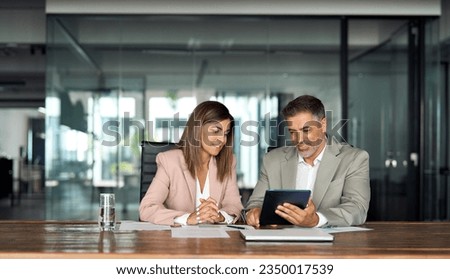 Professional business executives office team working using digital tablet computer sitting at table. Two middle aged colleagues company board discussing smart technology at corporate meeting. Royalty-Free Stock Photo #2350017539