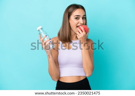Young caucasian woman isolated on purple background with a bottle of water and eating an apple Royalty-Free Stock Photo #2350021475