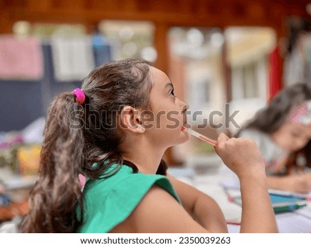 In the comforting environment of her home, a girl deep in thought holds a pen to her chin while studying. This candid moment encapsulates the essence of homeschooling. Royalty-Free Stock Photo #2350039263