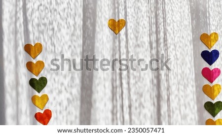 Multicolored hearts made of rough velvet paper on white surface with stripes of shadow and light from the sun. Abstract background, texture, copy space