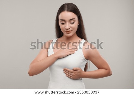 Beautiful young woman doing breast self-examination on light grey background Royalty-Free Stock Photo #2350058937