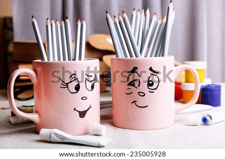 Emotional cups with pencils and paints on table