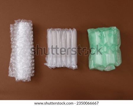 A pimply bag, and air cushions for packing fragile parcels on a brown background. Various types of polypropylene packaging bags. Bubble wrap and perforated airbags for transporting goods.  Royalty-Free Stock Photo #2350066667