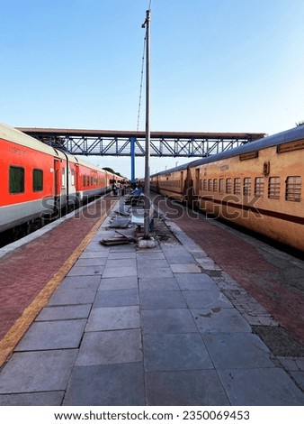At a rural railway station in Gujarat, India, two Indian railway trains stand facing each other with a diverse tapestry of passengers. People using bridge to arrive and exit the railway station. Royalty-Free Stock Photo #2350069453