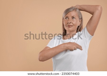 Beautiful senior woman doing breast self-examination on light brown background. Space for text Royalty-Free Stock Photo #2350074403