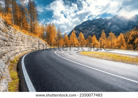 Road in mountains at sunny day in golden autumn. Dolomites, Italy. Beautiful roadway, orange tress, high rocks, blue sky with clouds. Landscape with empty highway through the mountain pass in fall Royalty-Free Stock Photo #2350077483