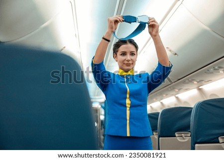 Female flight attendant in air hostess uniform holding seatbelt while standing near passenger seats in airplane Royalty-Free Stock Photo #2350081921