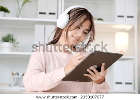 Happy young asian woman with headphones using digital tablet at home