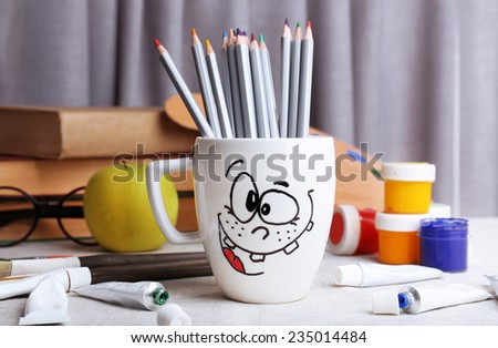 Emotional cup with pencils and paints on wooden table